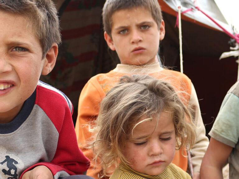 Children in a displacement camp in Syria hold a solar light