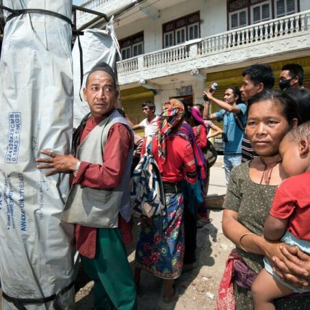 a street of people with a man holding a shelterbox relief pack