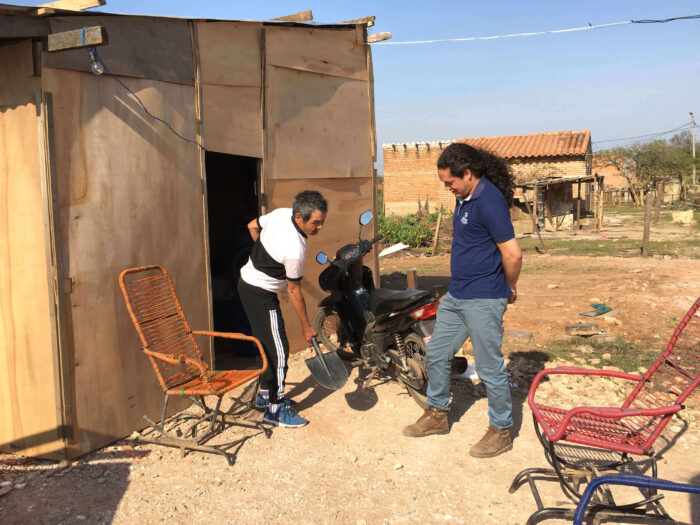 A man showing another man a shovel outside a home in Paraguay