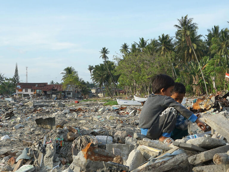 Indonesia children sitting on tsunami rubble