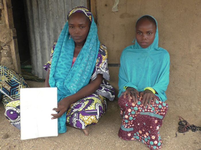 Two women wearing bright blue scarves sat down on the ground