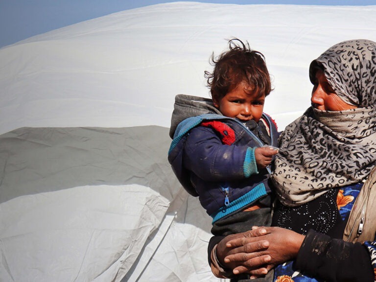 A woman holding a child in front of a tent