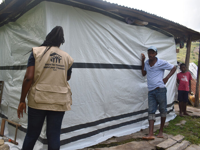 Three people in front of a home with tarpaulin
