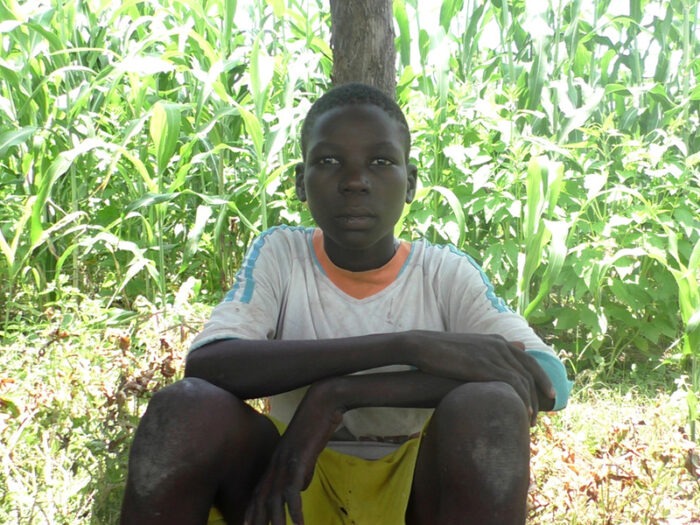 A young boy sat in front of a bush