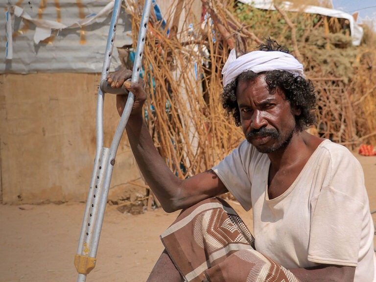 man sits in the sand with walking stick in yemen