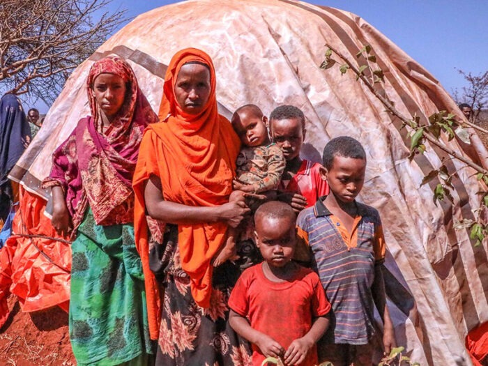 Woman holding a baby and four children standing outside of a shelter in Ethiopia