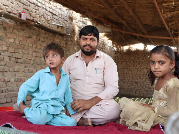 Man sitting on the floor with two children inside a shelter in Pakistan
