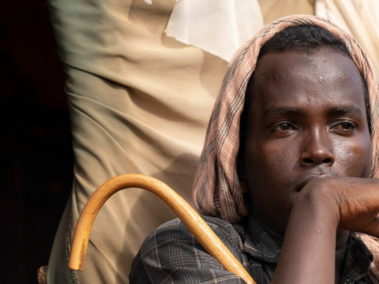 Portrait of a man holding a stick sitting outside of a tent