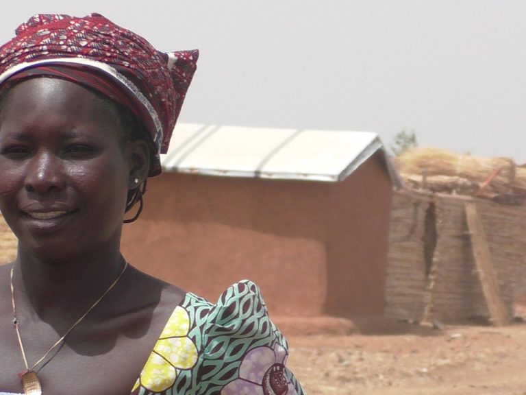 Woman wearing red scarf in her hair outside homes in Cameroon
