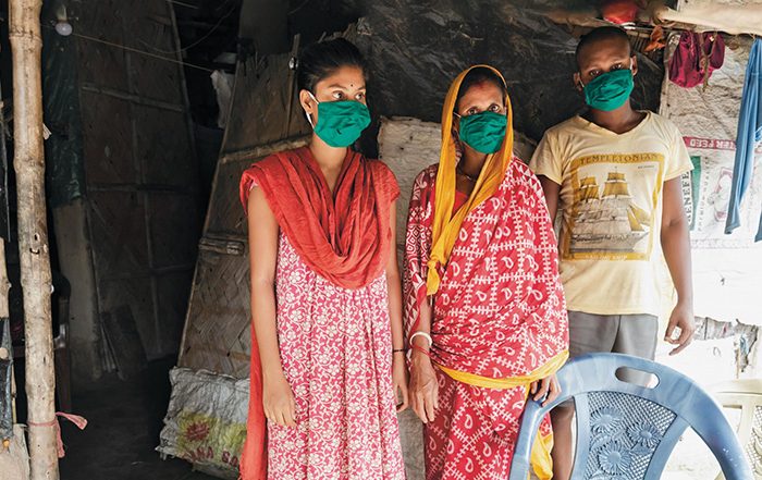 Three people wearing facemasks in a home in India