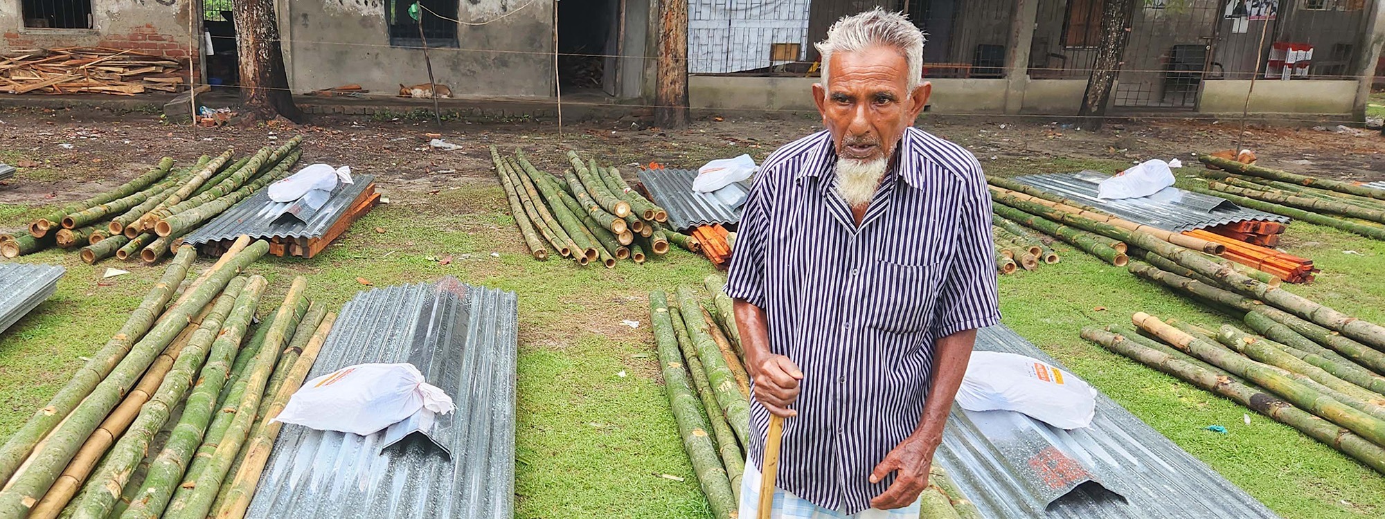 Elderly man standing next to piles of wood and metal in Bangladesh