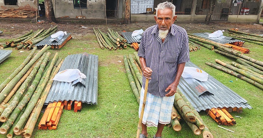 Elderly man standing next to piles of metal and wood in Bangladesh