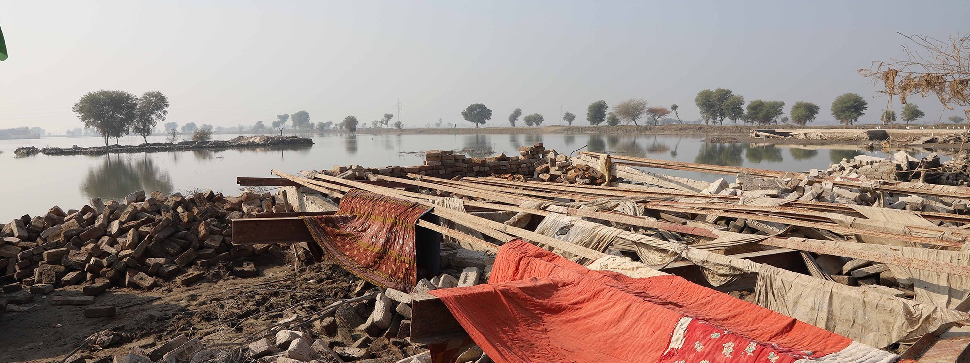 Flooded landscape next to rubble and cloths laid out to dry in Pakistan