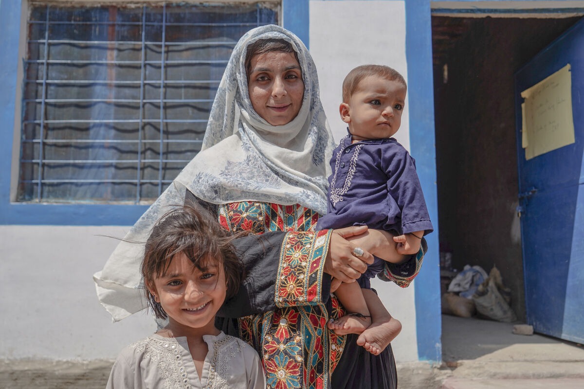 Woman holding a child next to another child outside a home in Pakistan