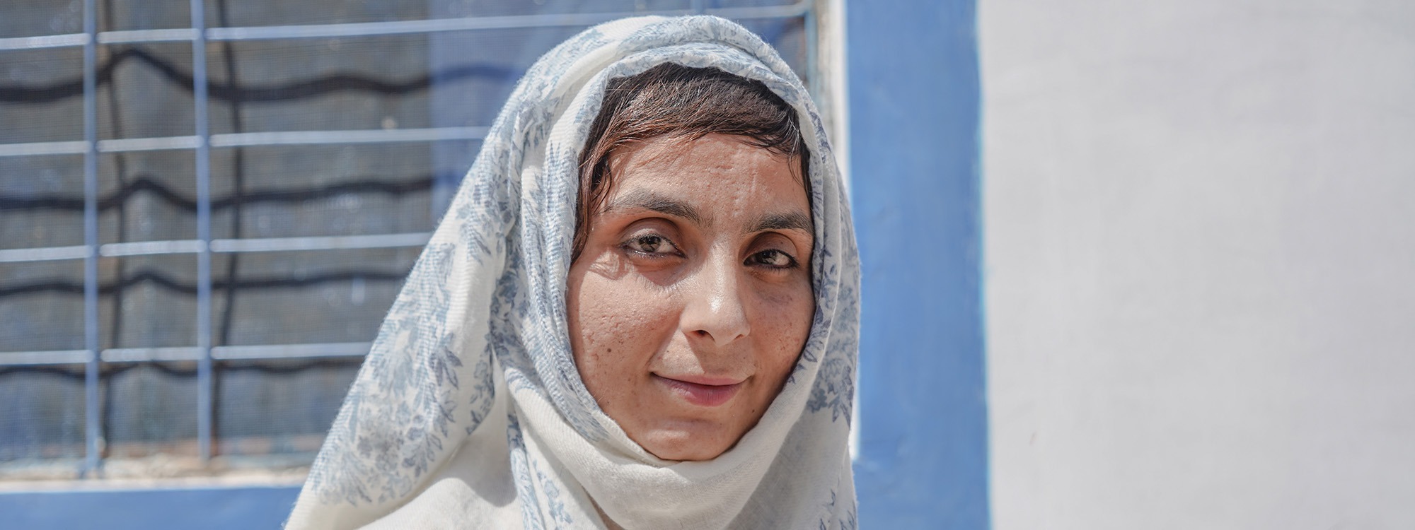 Woman wearing white and blue headscarf smiling at the camera