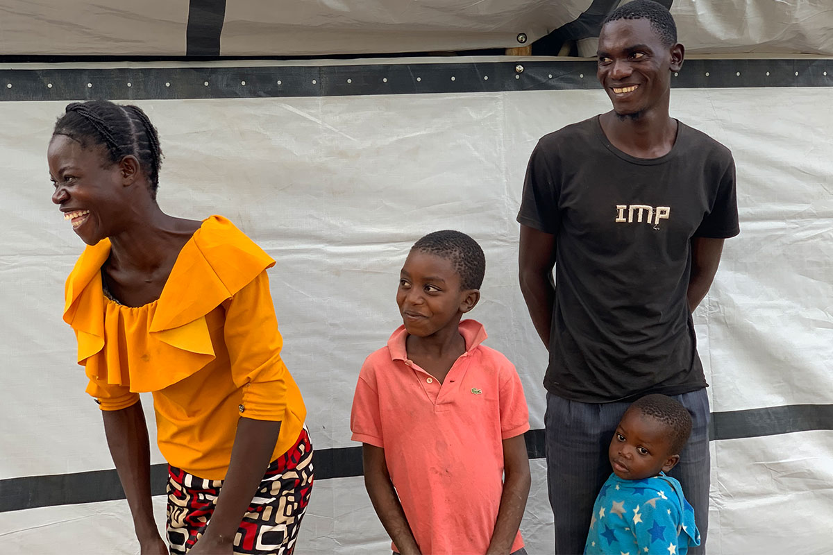 A family of four laughing in front of a temporary shelter in Malawi