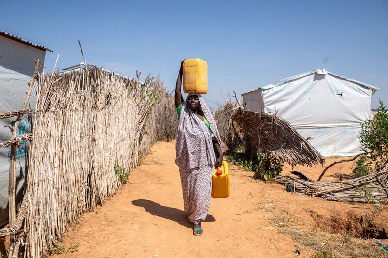 A woman walks back to her temporary shelter, after filling up water containers.