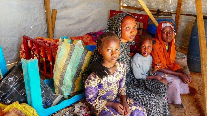 A family looking at the camera, sitting in a shelter in Chad, after fleeing the Sudan war.