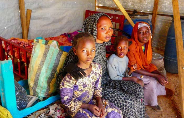 A family looking at the camera, sitting in a shelter in Chad, after fleeing the Sudan war.