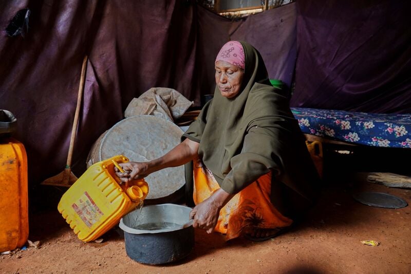A woman sat in a shelter with a jerry can pouring water.